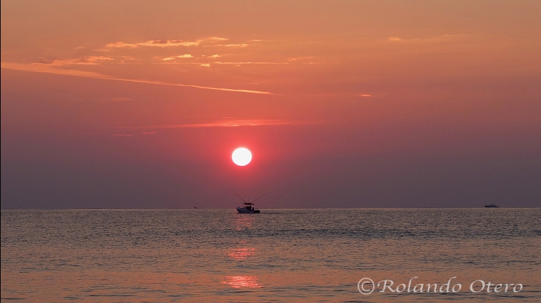 A boat offshore fishing drifts right into the sunrise.